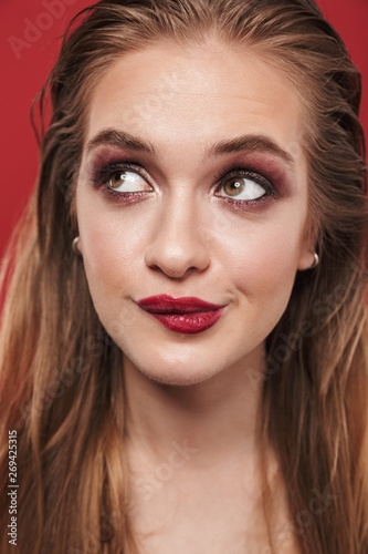 Beautiful young amazing woman with bright makeup red lipstick posing isolated over red wall background.