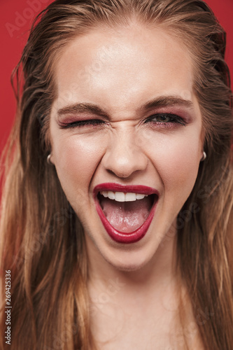 Beautiful young laughing happy emotional woman with bright makeup red lipstick posing isolated over red wall background.