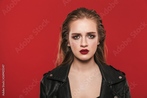 Beautiful young sad emotional woman with bright makeup red lipstick posing isolated over red wall background.