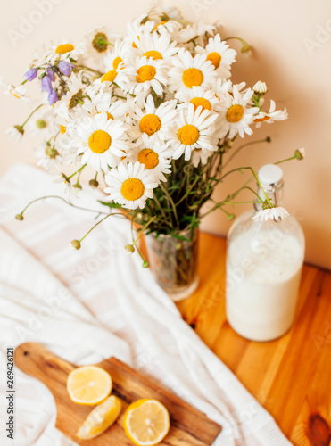 Simply stylish wooden kitchen with bottle of milk and glass on table, summer flowers camomile, healthy foog moring concept close up