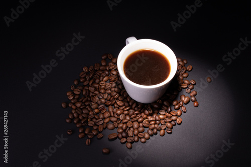 A beam of light is directed at a cup of coffee standing in a pile of coffee beans.
