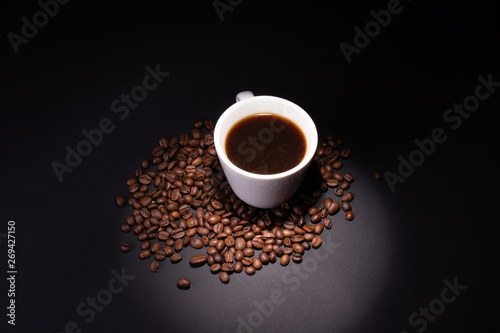Coffee grains among which there is a cup illuminated by a limited beam from the top
