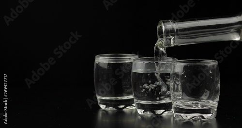 Pouring up shots of vodka from a bottle into glass against black background