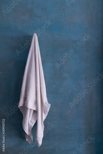 White towel hanging on ocean blue cement wall after shower.