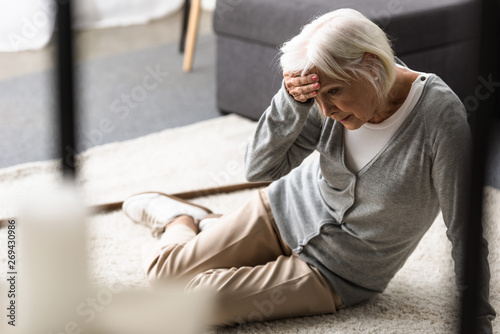 senior woman with migraine sitting on carpet and touching forehead with hand photo