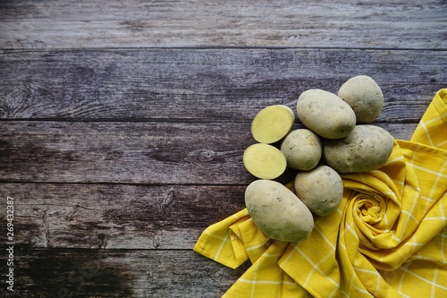 Fresh Potatoes on a yellow weathered cloth over a wooden background, top view