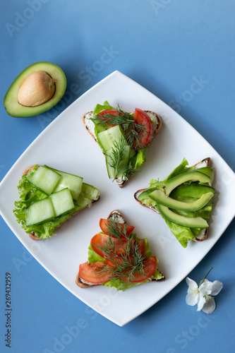 Vegetarian sandwiches with avocado, tomatoes and cucumbers on a blue background