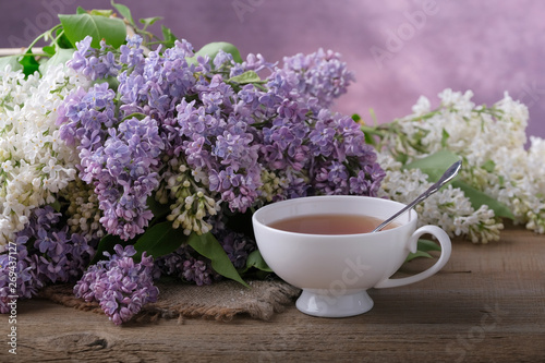 Bouquet of lilac, a cup of tea on a wooden table.
