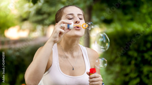 Closeup portrait of beautiful smiling young woman blowing soap bubbles in park at sunset