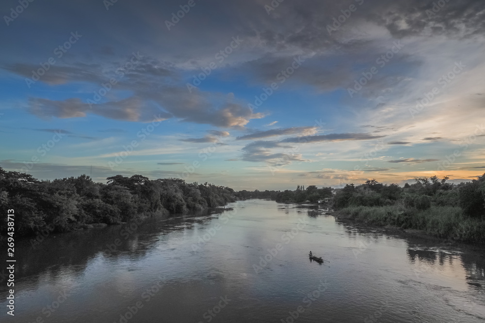river view evening of a fishing boat floating in Mae Klong river around with forest on both bank with cloudy sky background, Ban Pong District, Ratchaburi, Thailand. river view evening of a fishing boat floating in Mae Klong river around with forest on both bank with cloudy sky background, Ban Pong District, Ratchaburi, Thailand.