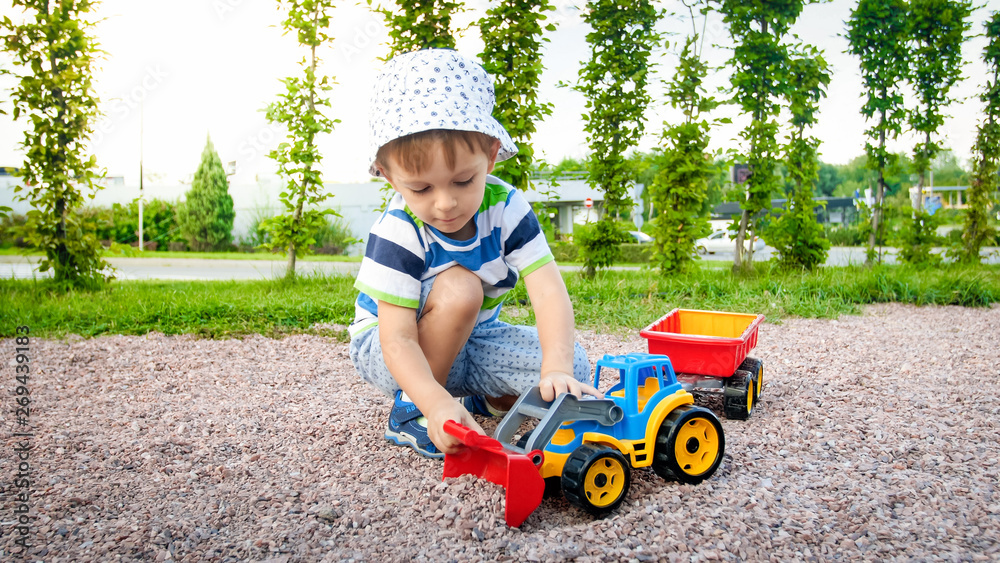 Closeup image of cute little boy playing on the palyground with toys. Child having fun with truck, excavator and trailer. He is pretending to be a builder or driver Closeup image of cute little boy playing on the palyground with toys. Child having fun with truck, excavator and trailer. He is pretending to be a builder or driver