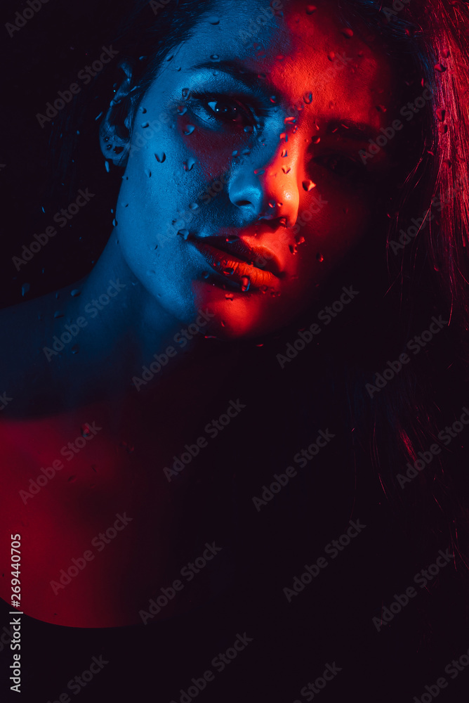 Sensual portrait of beautiful girl behind glass with raindrops with red blue lighting Sensual portrait of beautiful girl behind glass with raindrops with red blue lighting