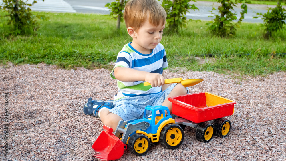 Photo of adorable 3 years old toddler boy playing with sand and you truck and trailer in park. Child digging and building in sandpit Photo of adorable 3 years old toddler boy playing with sand and you truck and trailer in park. Child digging and building in sandpit