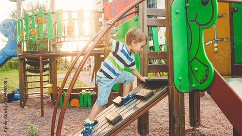 Photo of adorable toddler boy climbing and crawling on wooden staircase on children palyground at park photo