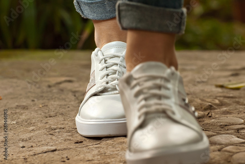 Female legs close-up. Sports sneakers on asphalt against green plants. Shoes in a tropical climate arranger.
