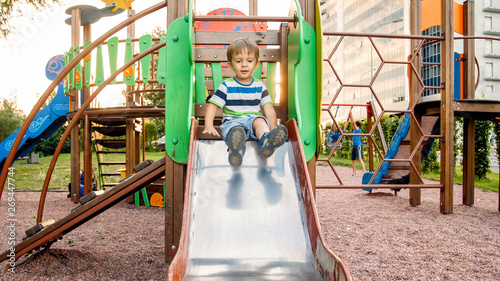 Obraz na płótnie Photo of cute 3 years old toddler boy climbing and riding on big slide on childr