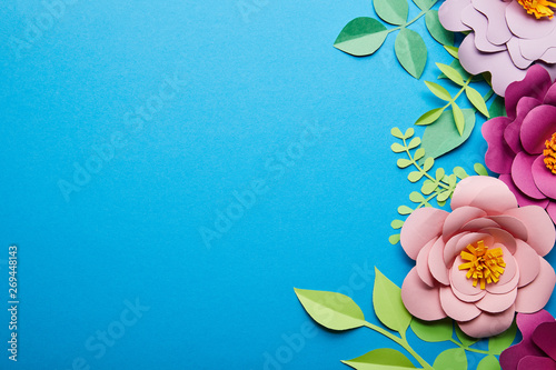Fototapeta Naklejka Na Ścianę i Meble -  top view of colorful paper cut flowers with green leaves on blue background with copy space