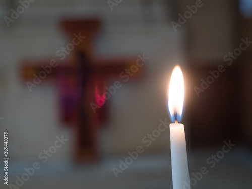 A candle and flame burn in a church with a blurred cross in the background.A single candle lit symbolises remembrance of a loved one who is deceased. tony skerl.