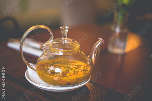 Close-up transparent glass teapot with sea buckthorn tea on the table in the restaurant