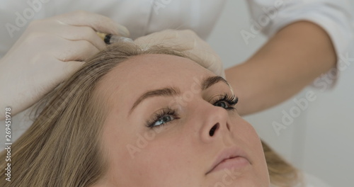 Young attractive woman receives mesotherapy for hair. Girl receives an injection in the head. Close up.