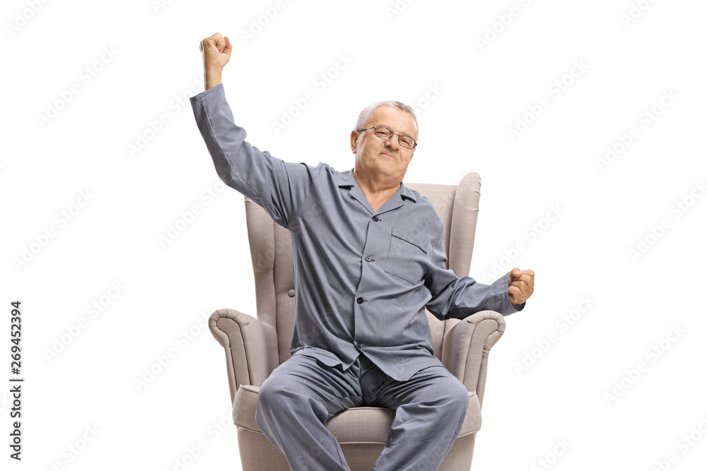 Mature man in pyjamas sitting in an armchair and stretching Mature man in pyjamas sitting in an armchair and stretching