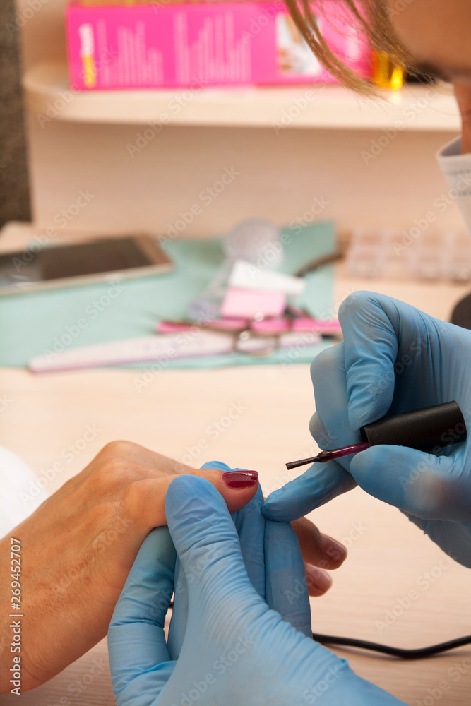 A manicurist in blue gloves puts a red gel polish on the womenl's nails.