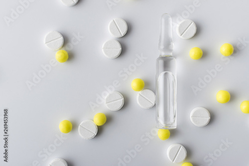 medical ampoule next to white and yellow pills of medical drugs and vitamins are in the hospital on a white background