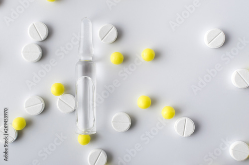 medical ampoule next to white and yellow pills of medical drugs and vitamins are in the hospital on a white background