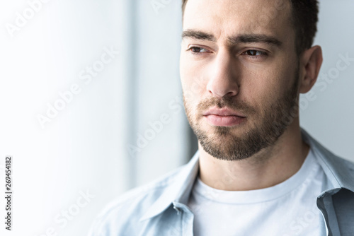 pensive bearded man in shirt looking away at home