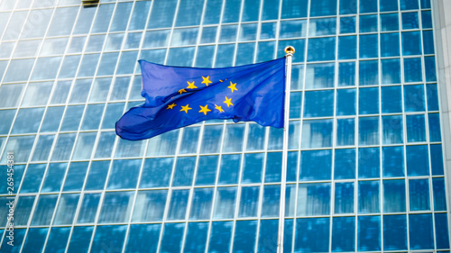 Image of EU flag fluttering on wind against high business office building made of concerete and glass. Concept of ecenomics, development, government and politics photo
