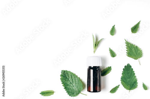 Herbal organic medicine product. Bottle of essential oil with fresh nettle and peppermint on white background. Flat lay, top view, copy space