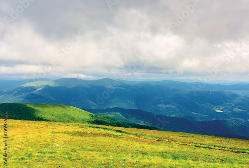 mountain landscape on a cloudy day. footpath through grassy meadow. mountain ridge in the distance. stormy weather in summer