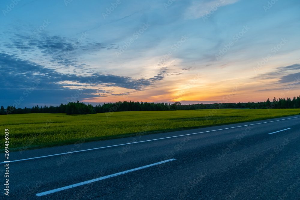 Beautiful, bright sunset on the background of the forest, the field and the asphalt road. Charming landscape at sunset. Beautiful, bright sunset on the background of the forest, the field and the asphalt road. Charming landscape at sunset.