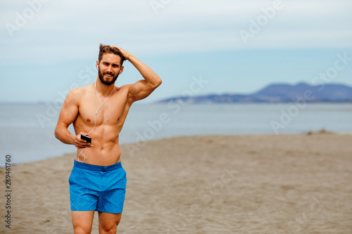 Canvas Print Handsome man on the beach listens to music over the earphones