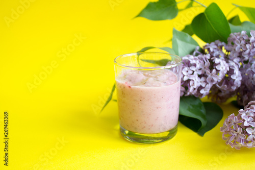 Fresh berry smoothie on a yellow background. A branch of lilac and berries smoothie
