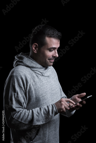 Studio portrait of a man touching a mobile phone. Isolated on black background. Vertical.