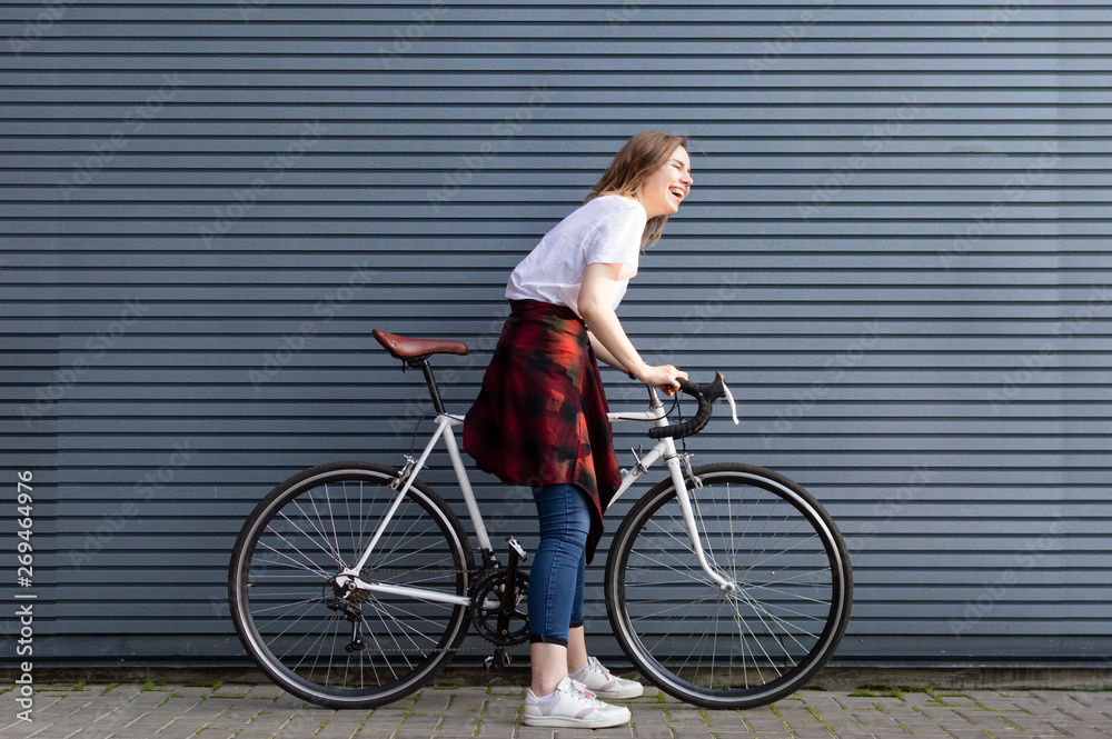 beautiful young girl standing with a white bicycle on a background of gray striped wall, the woman is happy beautiful young girl standing with a white bicycle on a background of gray striped wall, the woman is happy