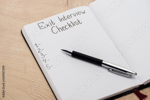 notebook with exit interview checklist lettering and numbers on wooden table with pen