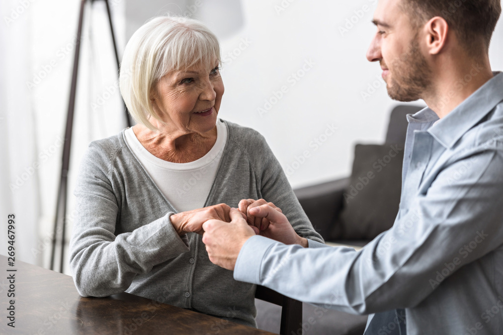 smiling man holding hands with senior mother a home smiling man holding hands with senior mother a home