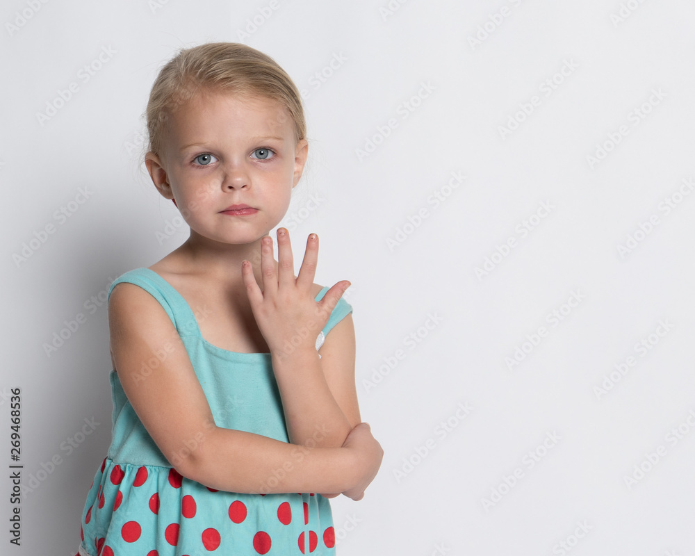 Young girl with blonde hair and blue eyes in flower print dress against white background Young girl with blonde hair and blue eyes in flower print dress against white background