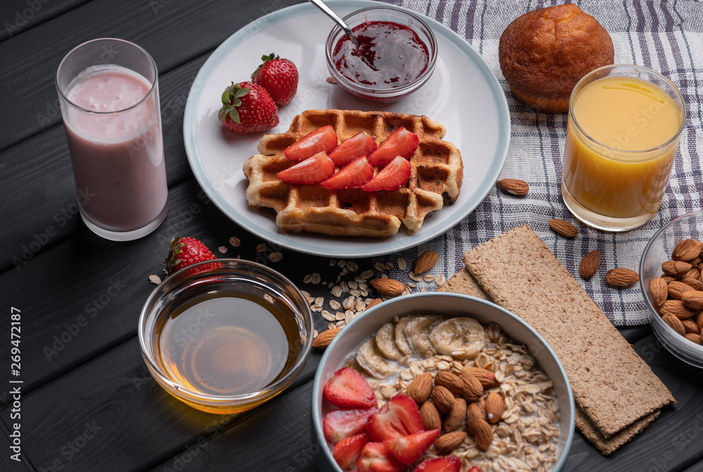 Oatmeal. Breakfast. Food. Muesli. Snack. Morning meal. Fresh waffles. Strawberry, honey, jam, almond and muffin on black table background Oatmeal. Breakfast. Food. Muesli. Snack. Morning meal. Fresh waffles. Strawberry, honey, jam, almond and muffin on black table background