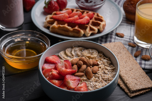 Oatmeal. Breakfast. Food. Muesli. Snack. Morning meal. Fresh waffles. Strawberry, honey, jam, almond and muffin on black table background