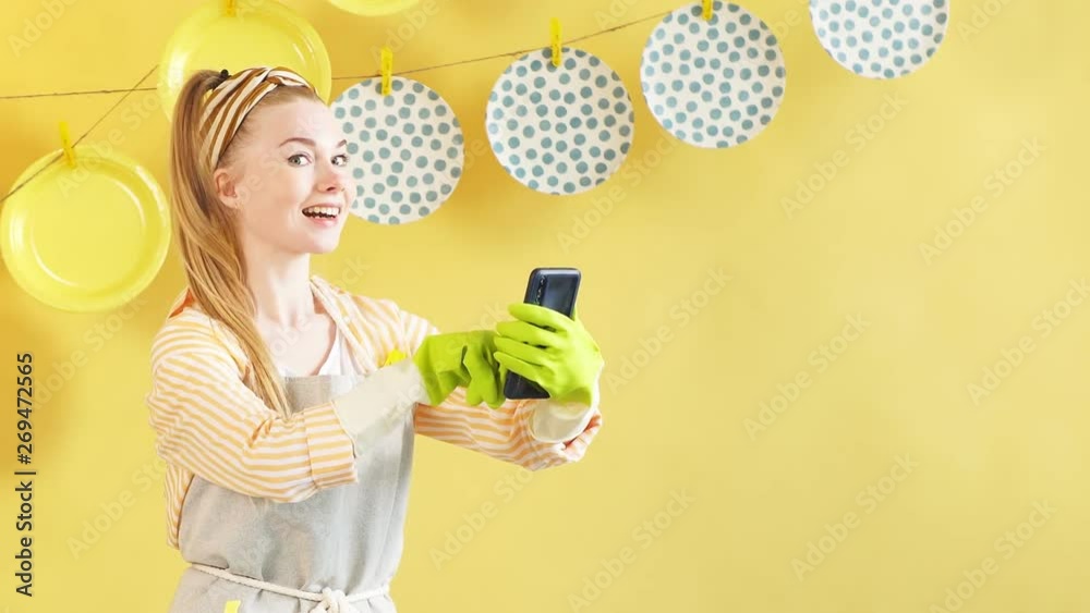 Cheerful positive blonde girl with raised finger and smartphone looking at camera. Happy housewife pointing up, holding a mobile phone and looking at the camera Cheerful positive blonde girl with raised finger and smartphone looking at camera. Happy housewife pointing up, holding a mobile phone and looking at the camera