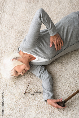 overhead view of sick senior woman with walking stick lying on carpet