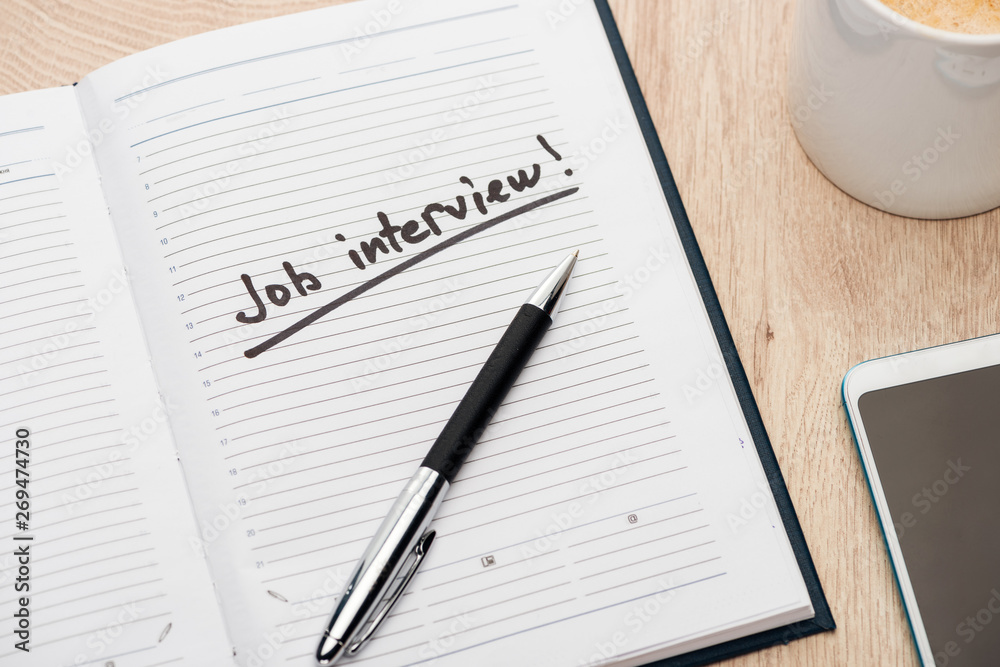 notebook with pen and job interview lettering on wooden table near smartphone and coffee cup notebook with pen and job interview lettering on wooden table near smartphone and coffee cup
