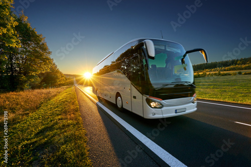 Canvas Print White bus traveling on the asphalt road around line of trees in rural landscape