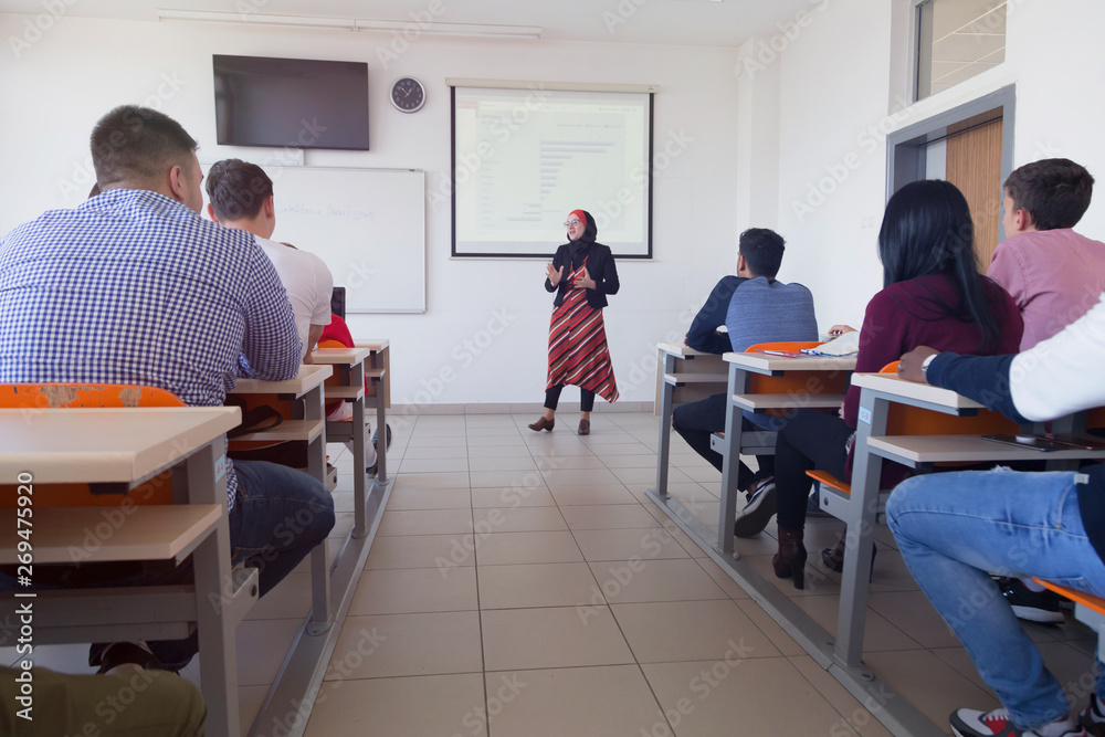Female muslim professor explain lesson to students and interact with them in the classroom.Helping a students during class. University student being helped by female lecturer during class. Female muslim professor explain lesson to students and interact with them in the classroom.Helping a students during class. University student being helped by female lecturer during class.