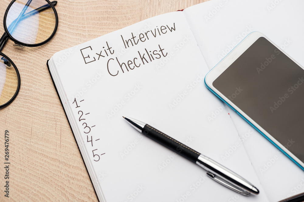 notebook with exit interview checklist lettering and numbers on wooden table near smartphone, pen and glasses notebook with exit interview checklist lettering and numbers on wooden table near smartphone, pen and glasses