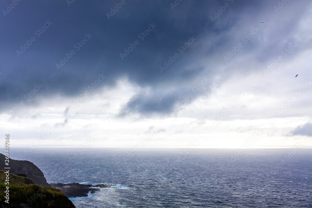 Dramatic sky over Atlantic Ocean coast near Sao Miguel Island, the largest island in the archipelago of the Azores, Portugal. Dark stormy clouds in the sky over the ocean