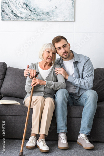man sitting on sofa and embracing senior mother
